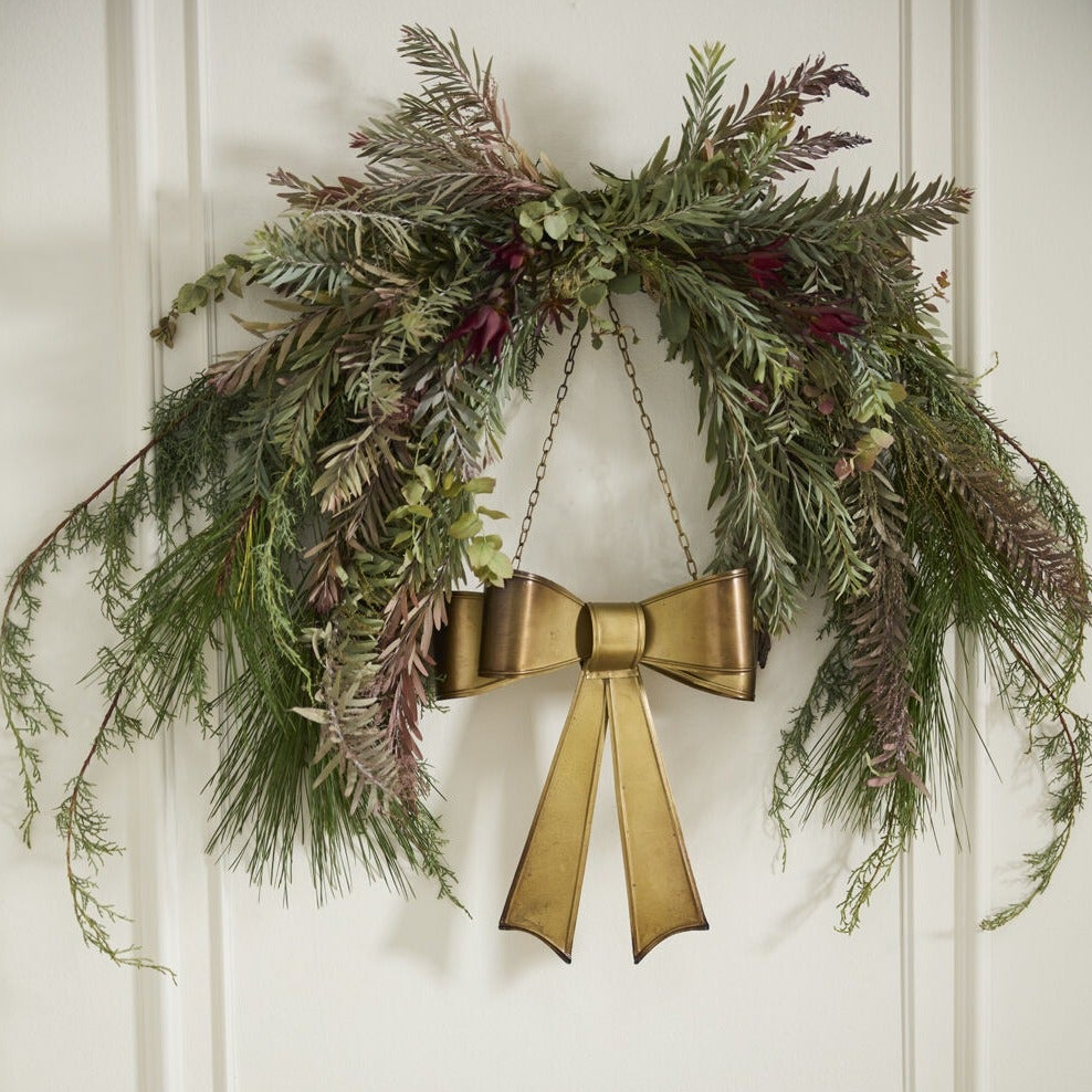 Decorative wreath with greenery and a gold bow on a white wall